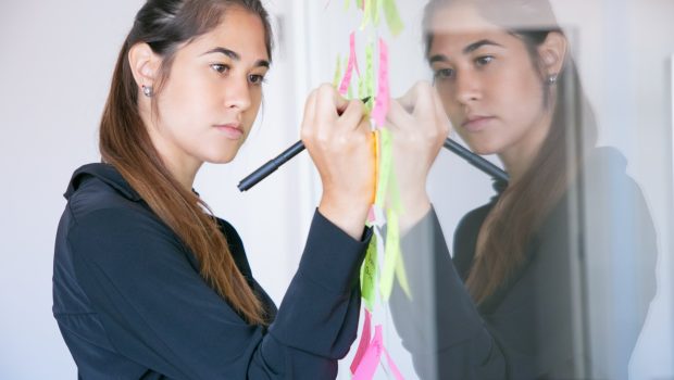 beautiful-young-latin-businesswoman-writing-on-sticker-with-marker-concentrated-professional-female-manager-sharing-idea-for-project-and-making-note-scaled.jpg